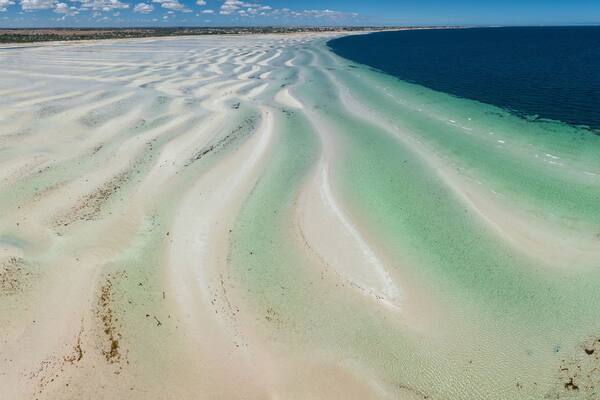 Panoramic view of white sand beach with ripples and pools of water in front alongside a blue ocean