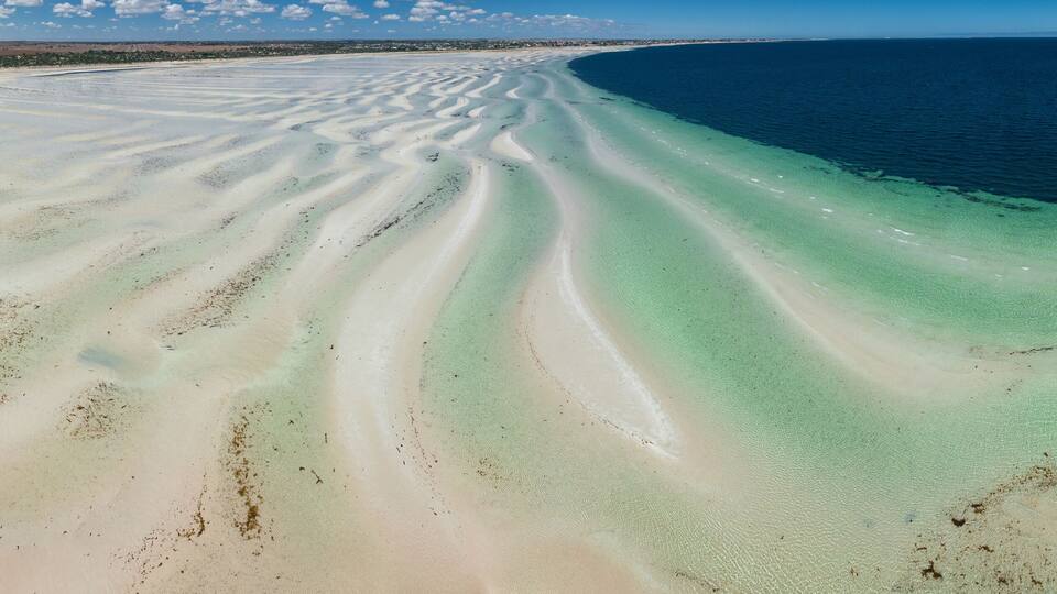 A coastal landscape with a wide sandy beach and clear blue waters.