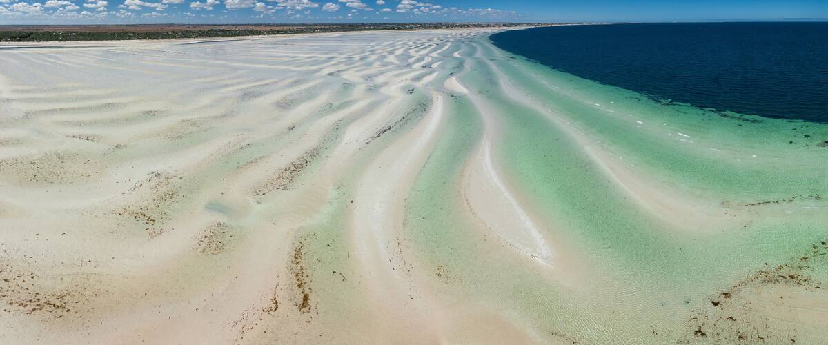 A coastal landscape with a wide sandy beach and clear blue waters.