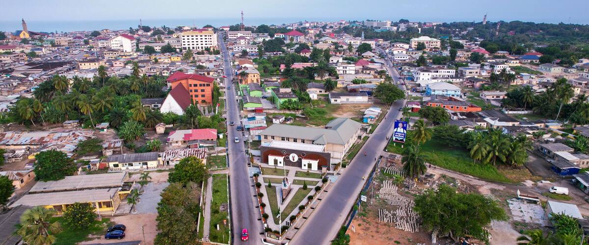 An aerial view of a city with a prominent road, various buildings, and palm trees.