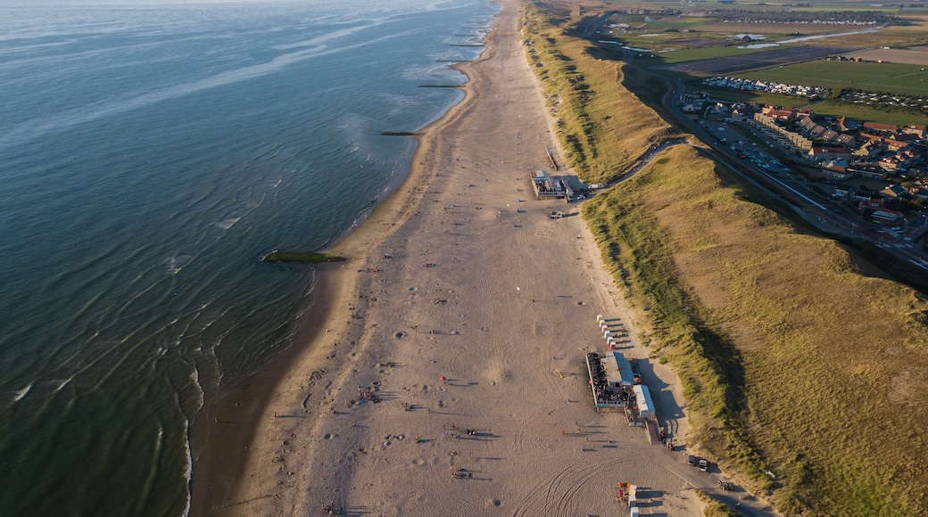 Vue aĂ©rienne dâune zone cĂŽtiĂšre avec une plage de sable, une route parallĂšle au rivage et un ensemble de bĂątiments situĂ©s sur la droite.