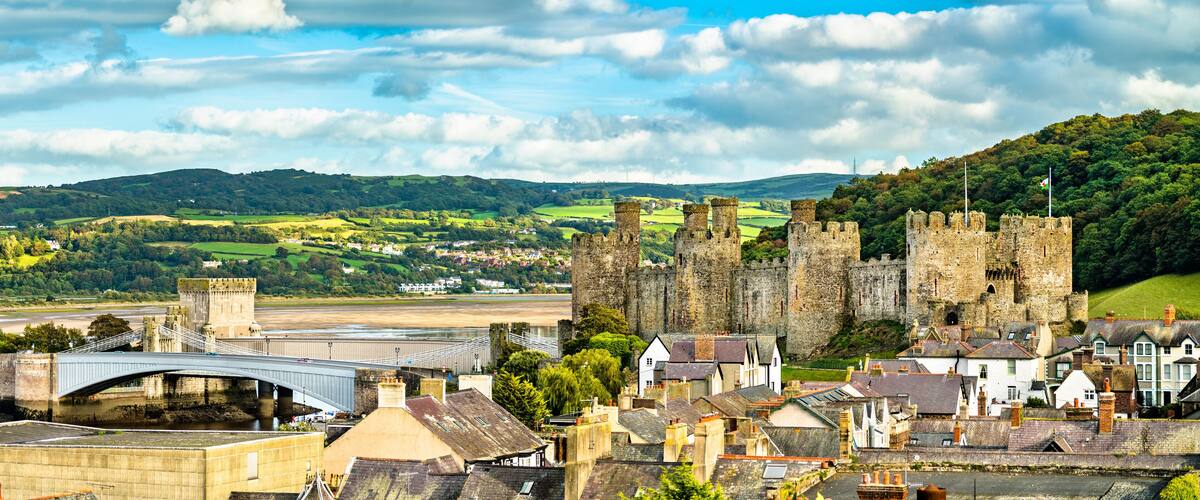 A historic castle, a river, and a modern bridge in a scenic landscape.
