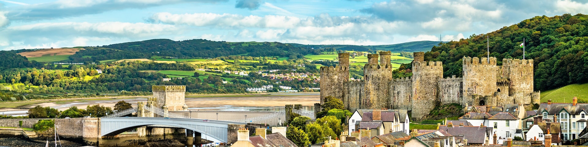 A historic castle, a river, and a modern bridge in a scenic landscape.