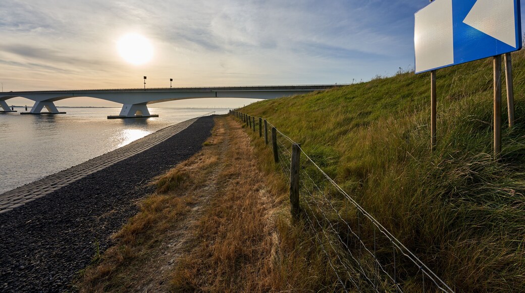 Zeeland bridge in Netherlands. Concrete and steel construction connecting the municipalities of Schouwen-Duiveland and Noord-Beveland. Pasture fence and traffic sign in foreground. Backlight shot.