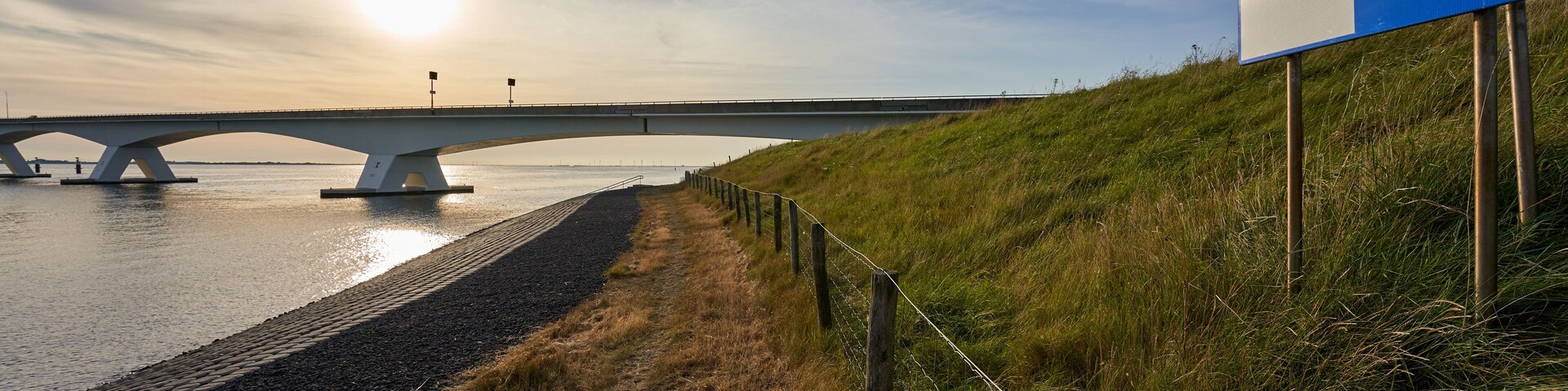 Zeeland bridge in Netherlands. Concrete and steel construction connecting the municipalities of Schouwen-Duiveland and Noord-Beveland. Pasture fence and traffic sign in foreground. Backlight shot.