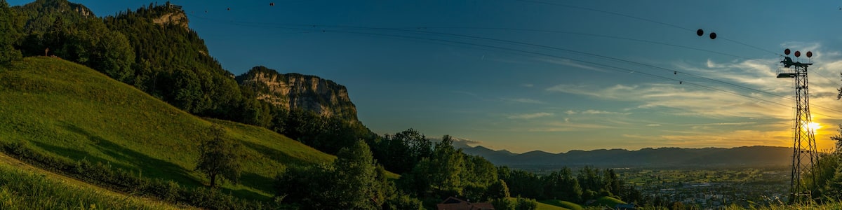 Sonnenuntergang über den Schweizer Bergen im Rheintal, Vorarlberg, Austria. leuchtendes Abendrot, tolle Stimmung mit roten und graublauen Wolken über den grünen Wiesen und Bäumen. Seilbahn zum Karren