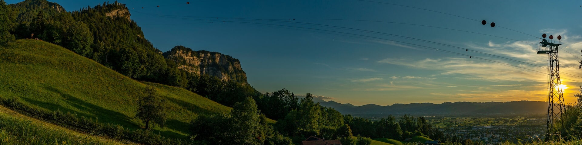 Sonnenuntergang über den Schweizer Bergen im Rheintal, Vorarlberg, Austria. leuchtendes Abendrot, tolle Stimmung mit roten und graublauen Wolken über den grünen Wiesen und Bäumen. Seilbahn zum Karren