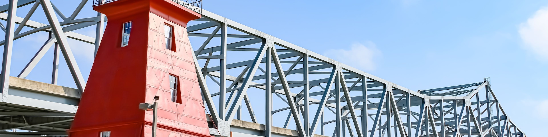 Ein roter Leuchtturm auf einer Stahlbrücke, strahlend blauer Himmel.