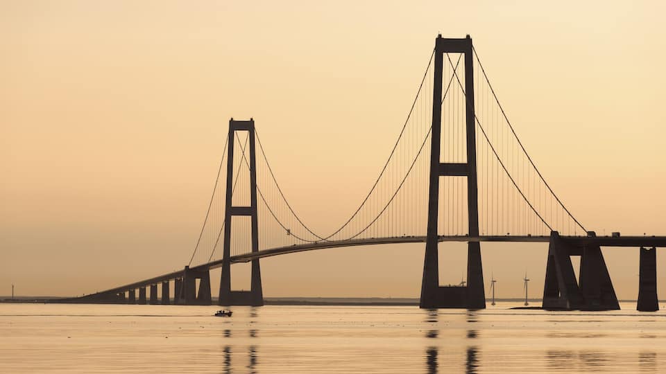 A large suspension bridge over calm water during sunset.