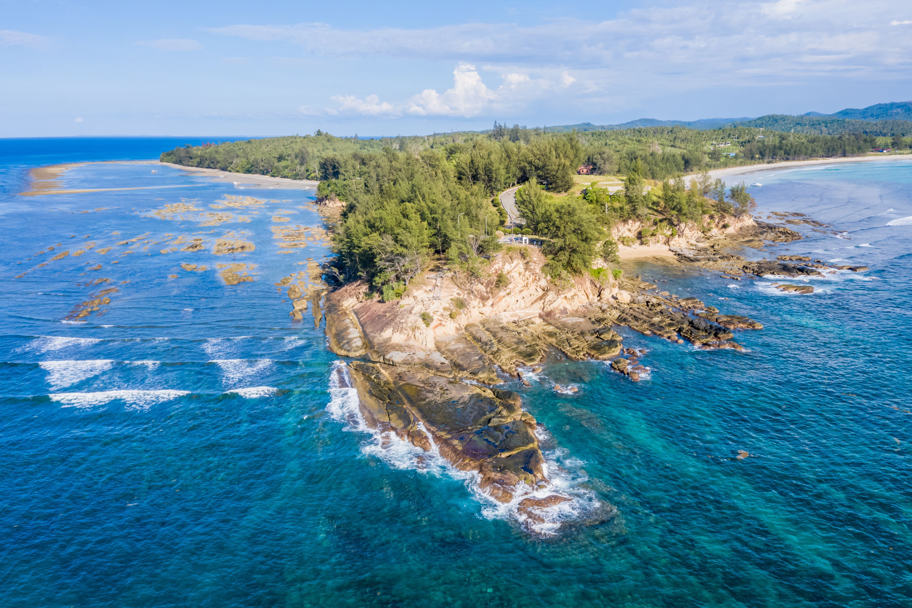 Un paysage côtier avec une île rocheuse entourée d’eaux bleues et limpides, une plage de sable et une zone forestière dense.