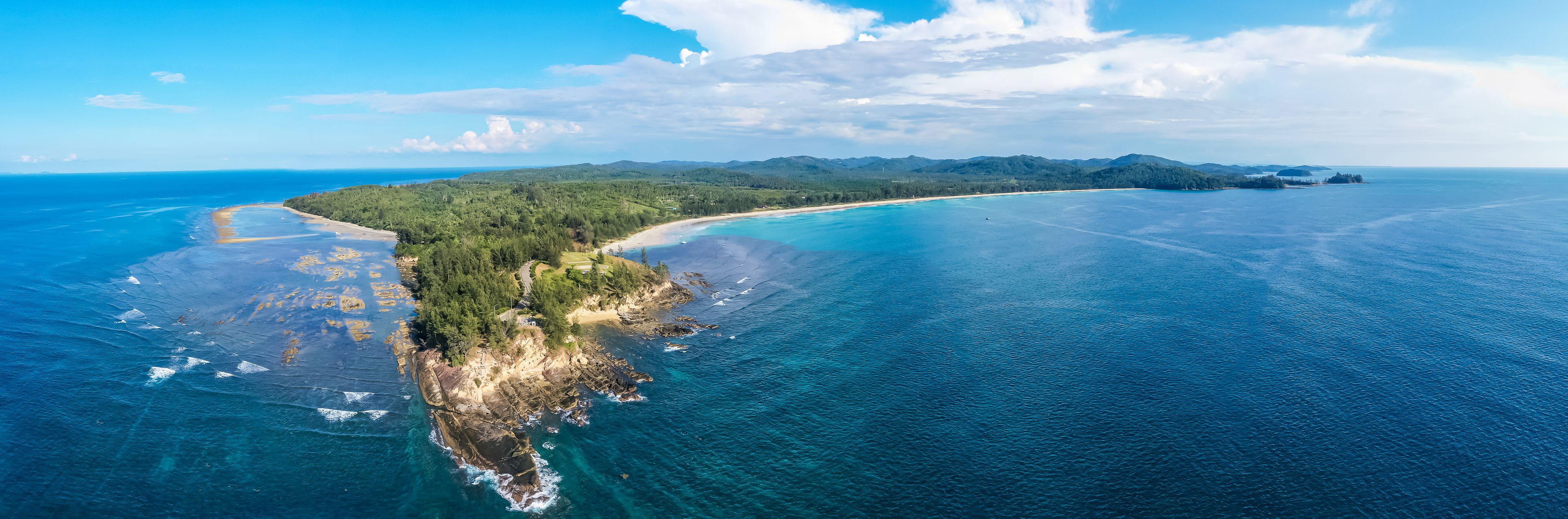 Un paisaje costero con mar azul cristalino, una playa arenosa y una península boscosa.