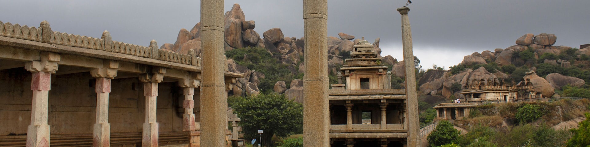 Ancient stone ruins with columns and a temple structure amidst rocky hills.