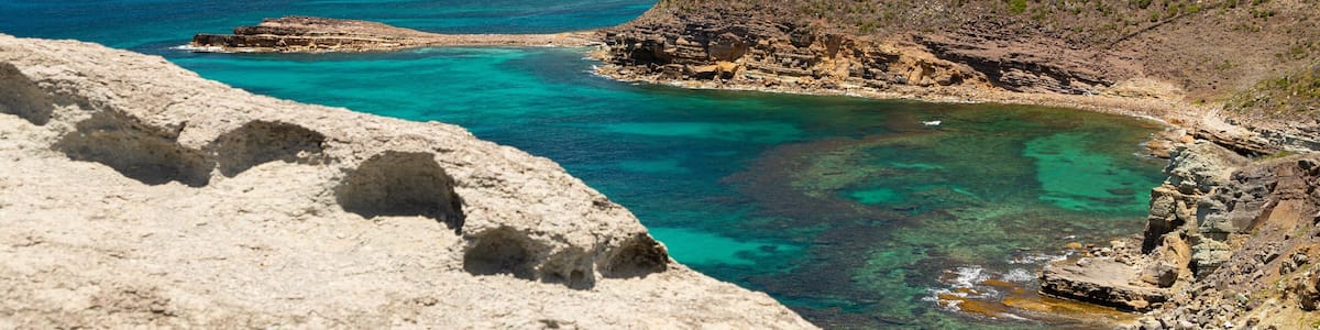 A coastal landscape with clear turquoise waters, rocky shores, and a hill with buildings.