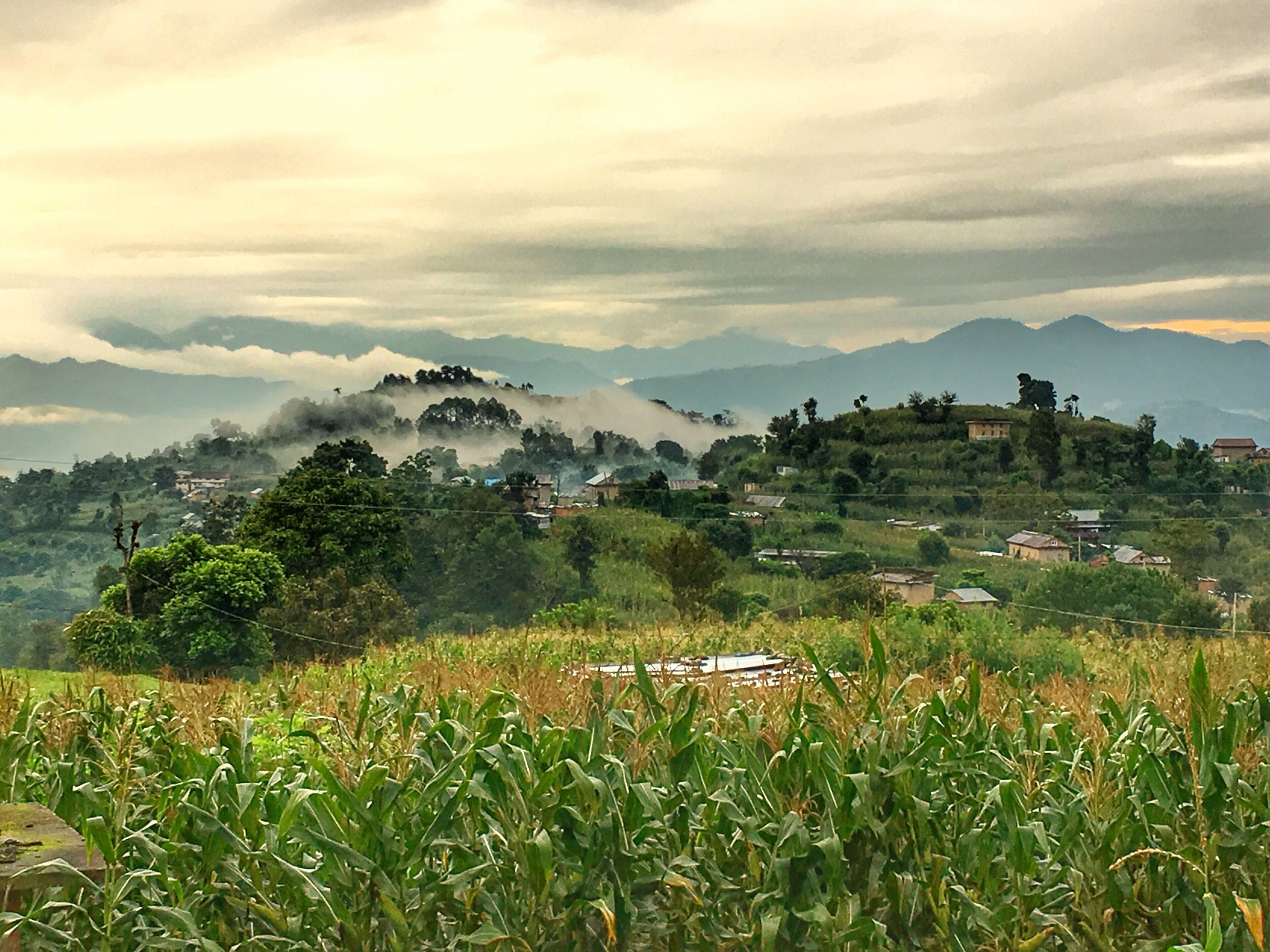 A rural landscape with a village nestled among rolling hills and mountains.