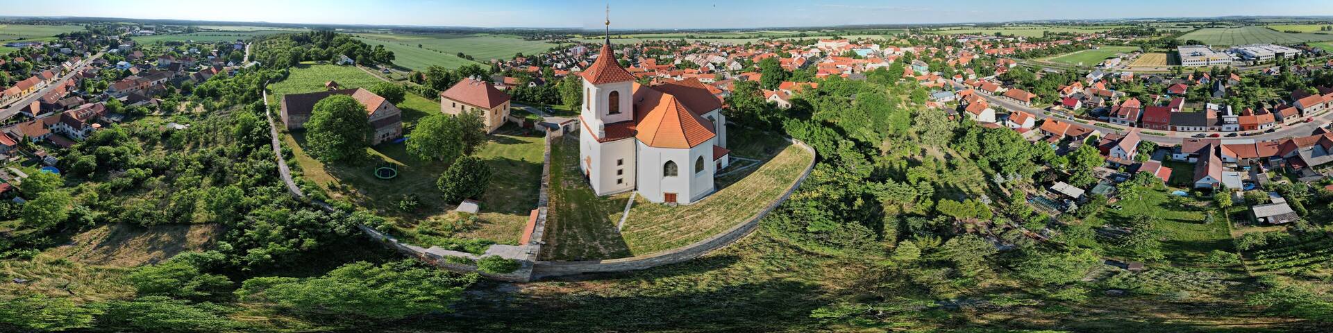 A town with a prominent church surrounded by greenery and a river.
