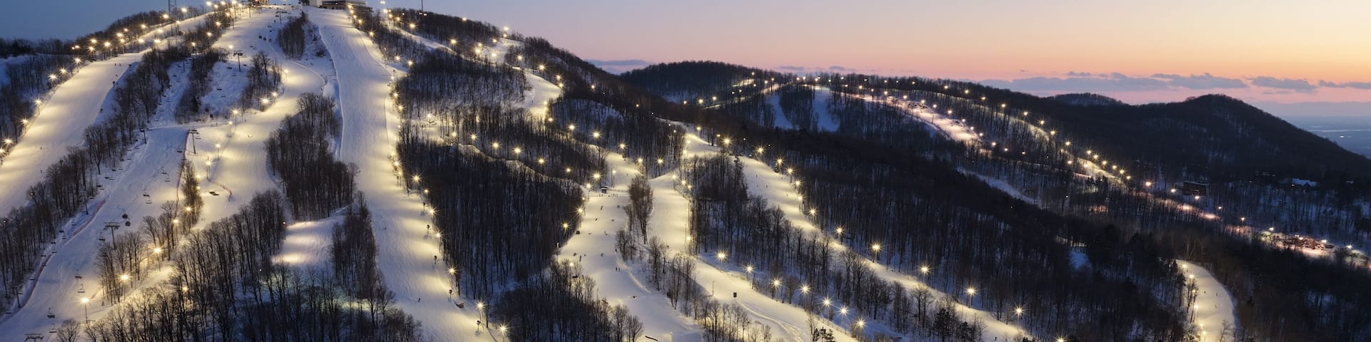 Aerial drone view of illuminated Bromont ski resort slopes at dusk, Quebec, Canada in winter. g.