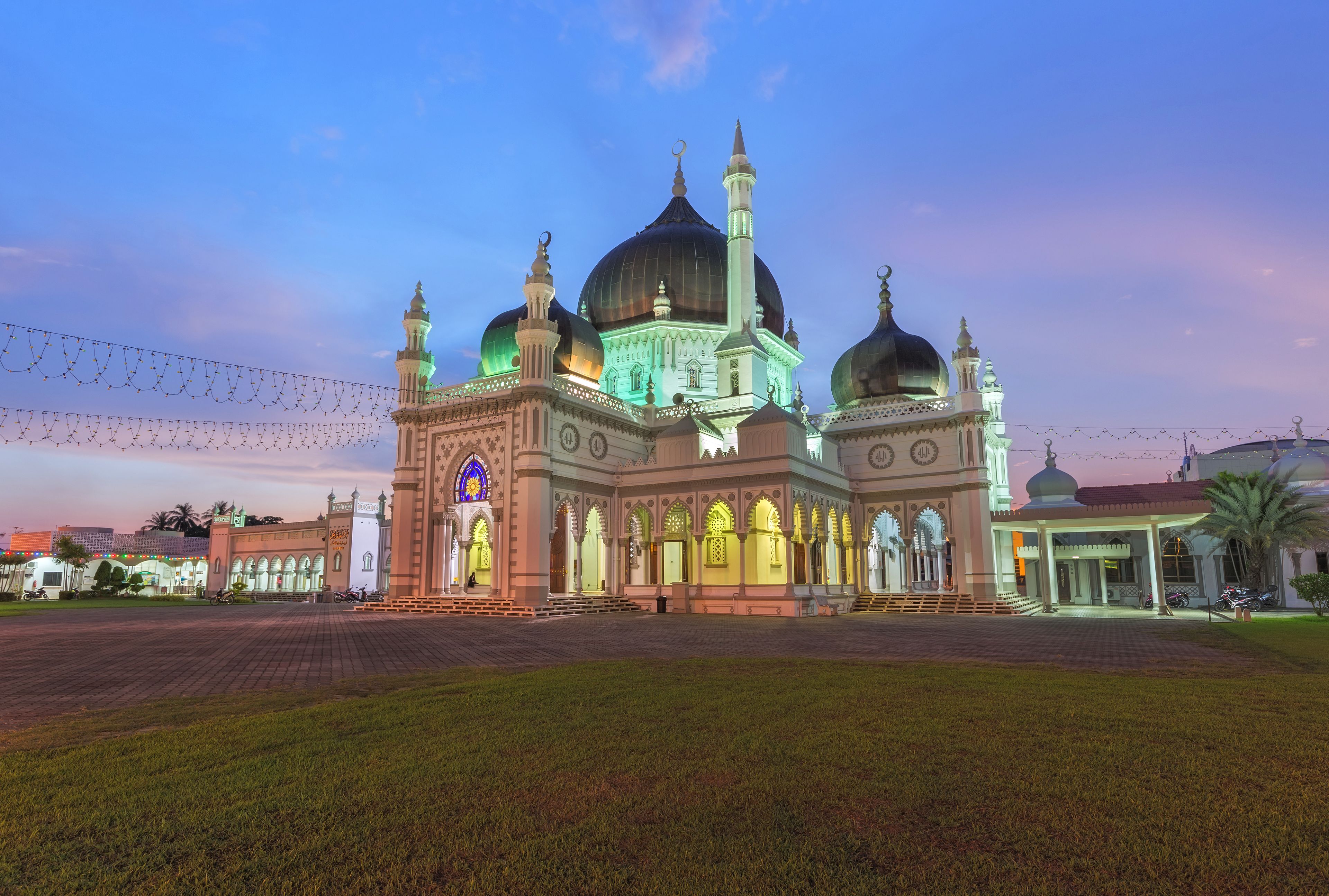 A mosque with multiple domes and minarets, surrounded by a paved area with string lights.