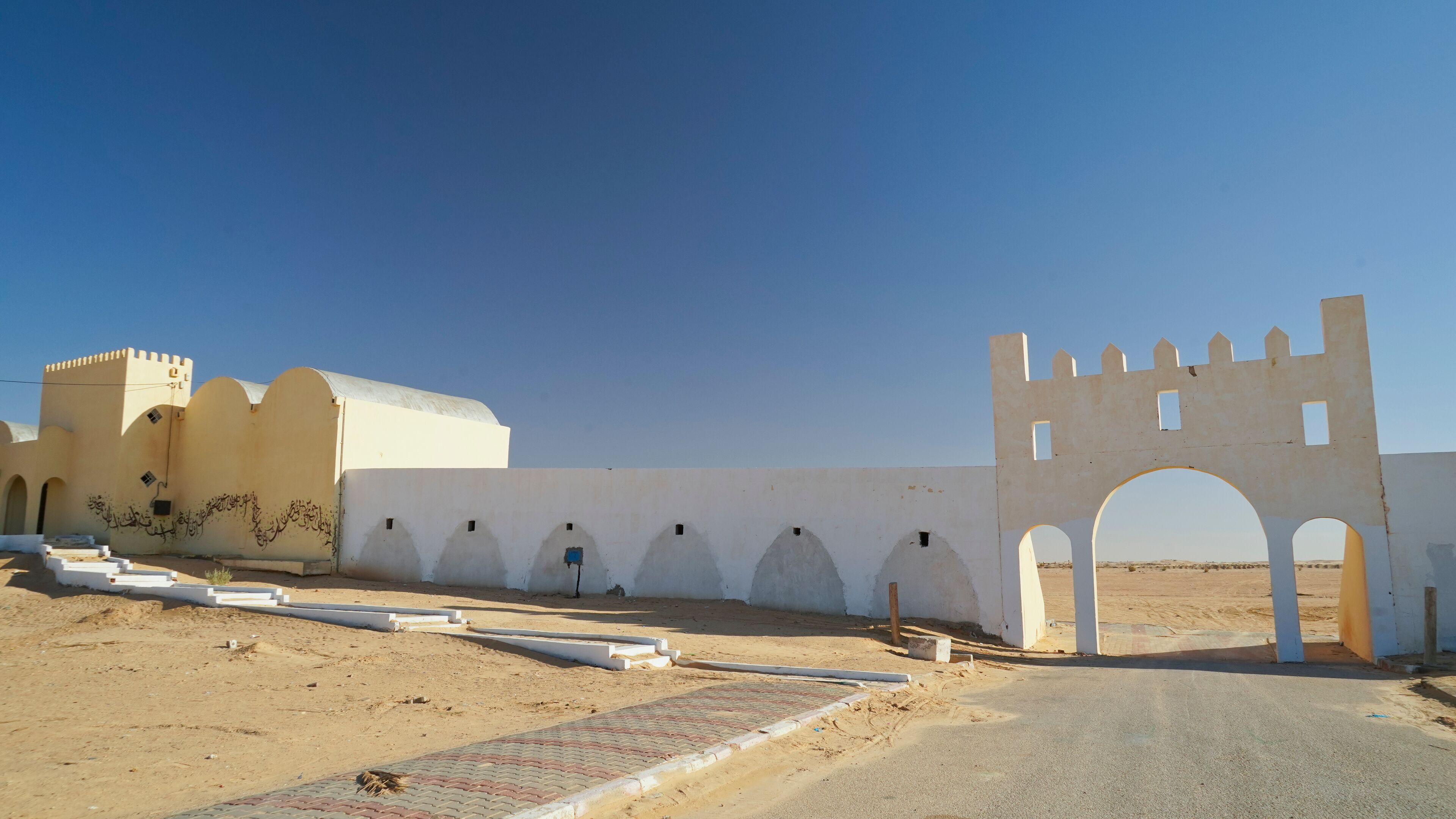 A desert landscape with a white wall featuring arched doorways and a castle-like structure.