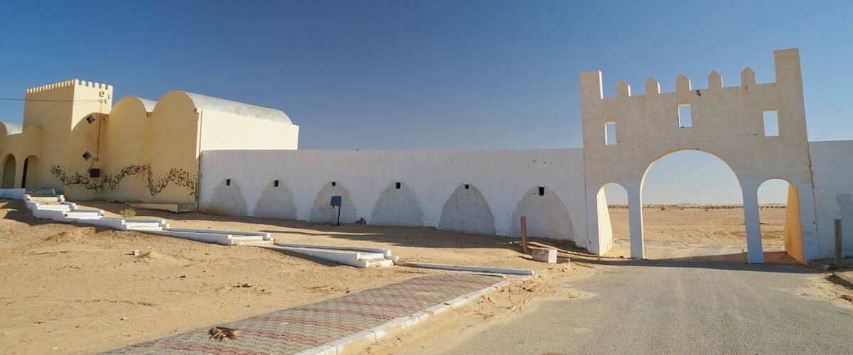 A desert landscape with a white wall featuring arched doorways and a castle-like structure.