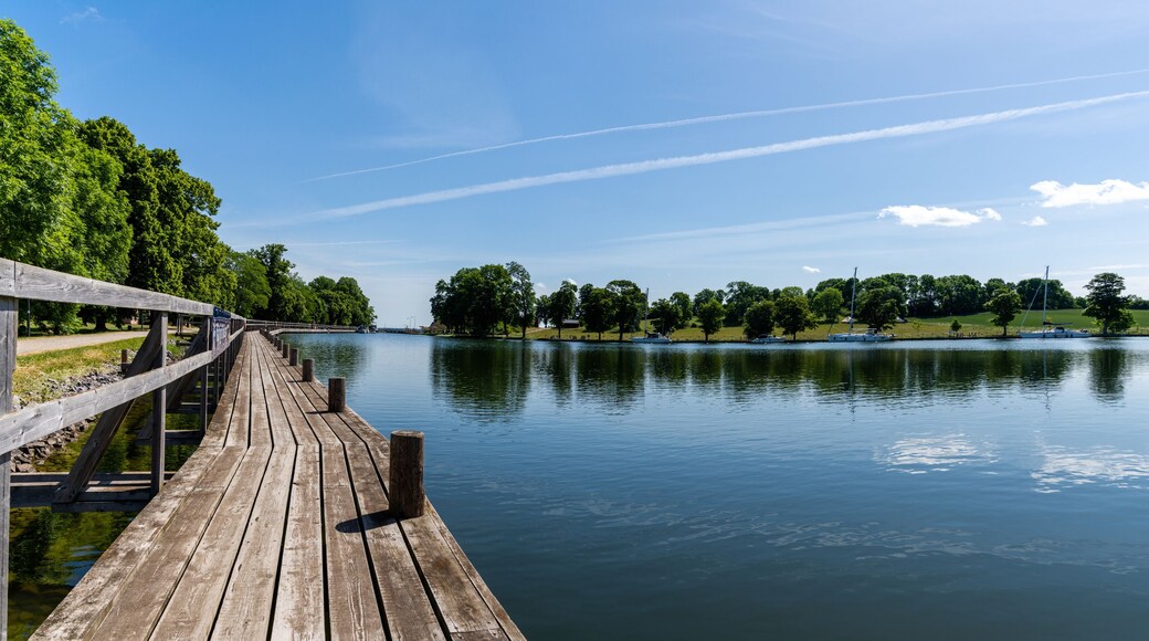 idyllic lake with a wooden boardwalk along the side and sailboats moored in the background