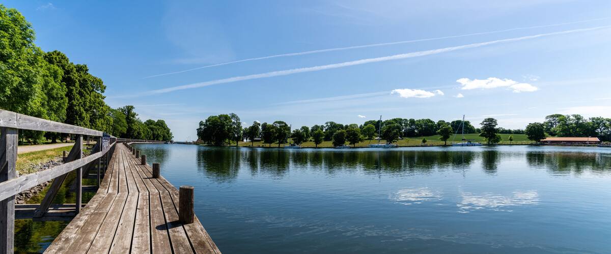 idyllic lake with a wooden boardwalk along the side and sailboats moored in the background