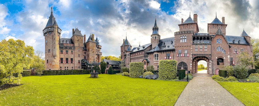 A large, historic brick castle with multiple towers and a well-maintained garden.