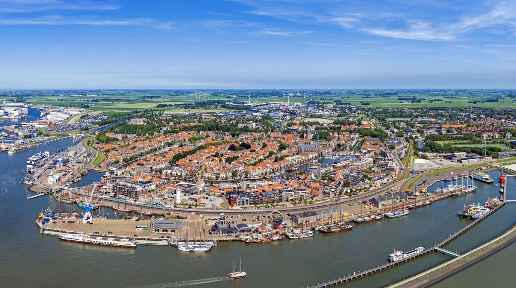 Luftaufnahme einer Küstenstadt mit Hafen, Windkraftanlagen und umliegenden grünen Feldern.