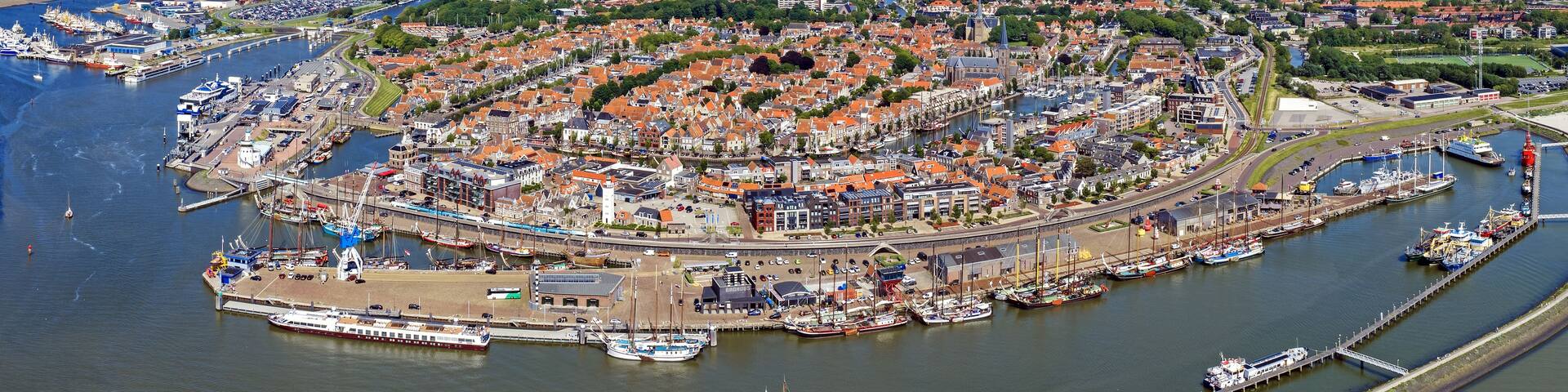 An aerial view of a coastal town with a harbor, wind turbines, and surrounding green fields.
