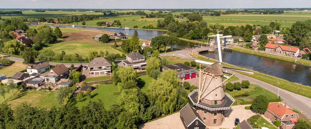 A riverside town with a prominent windmill, houses, and lush greenery.