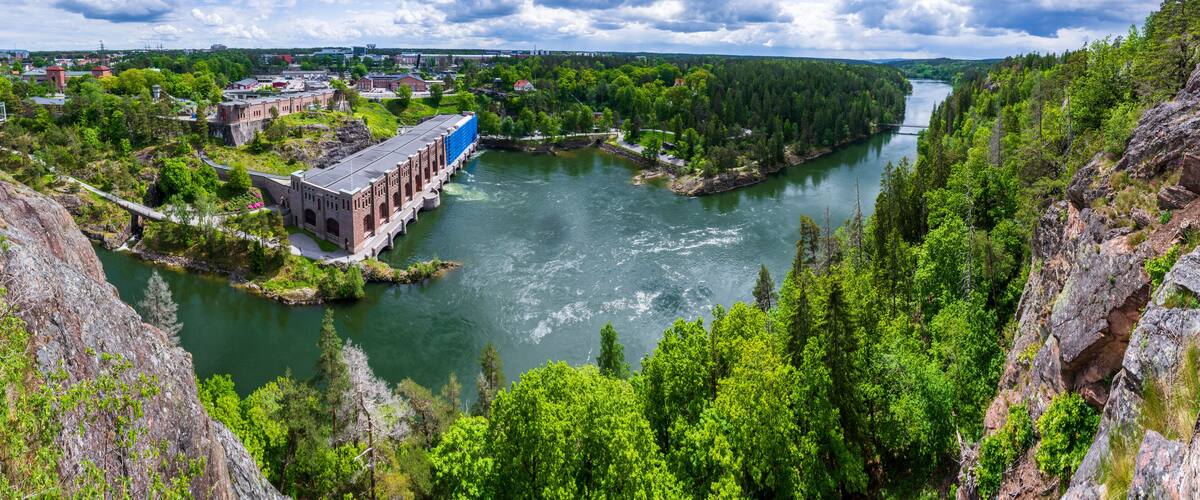 A river flowing through a forested valley with a bridge and buildings on the left.