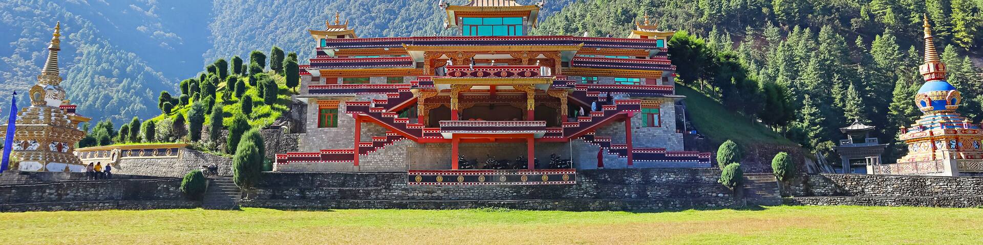A traditional multi-tiered temple with intricate architecture, surrounded by lush green hills and a clear blue sky.