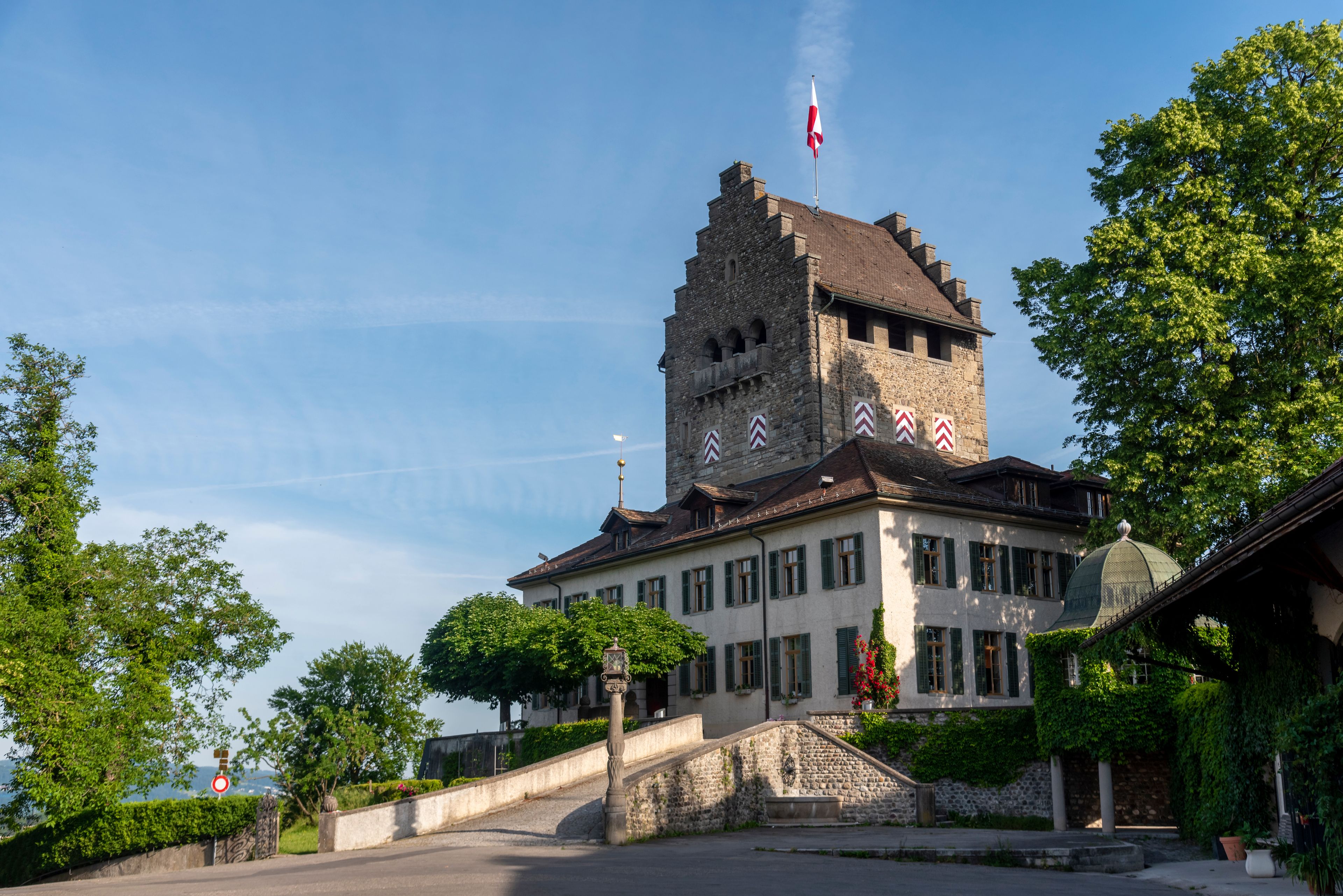 A historic building with a tower, surrounded by lush greenery and a clear sky.