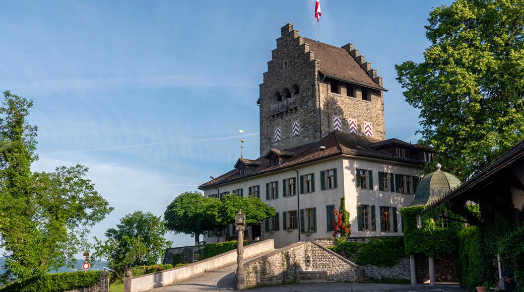 A historic building with a tower, surrounded by lush greenery and a clear sky.