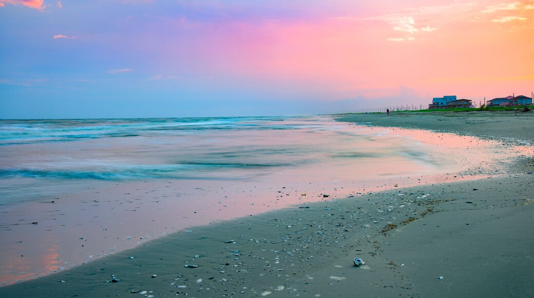 A beach with gentle waves, a clear sky, and houses in the background.