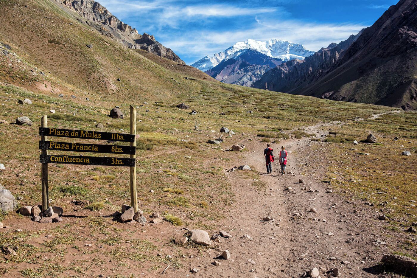 Sendero de montaña con un poste indicador de distancias a Plaza de Mulas, Plaza Francia y Confluencia.