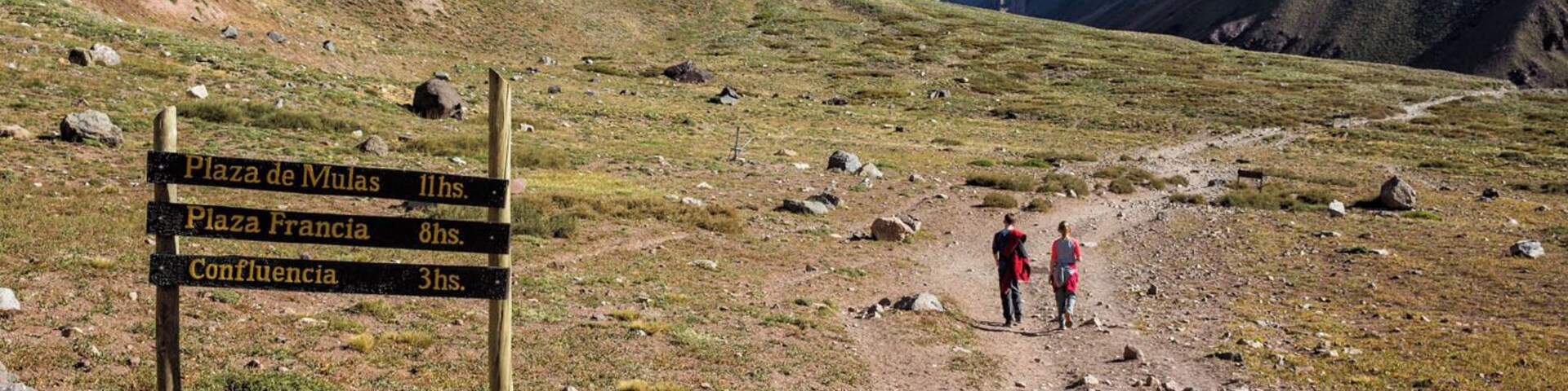 Sendero de montaña con un poste indicador de distancias a Plaza de Mulas, Plaza Francia y Confluencia.