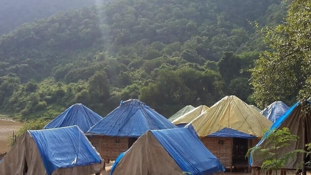 A campsite with several tents, surrounded by a forested hillside.