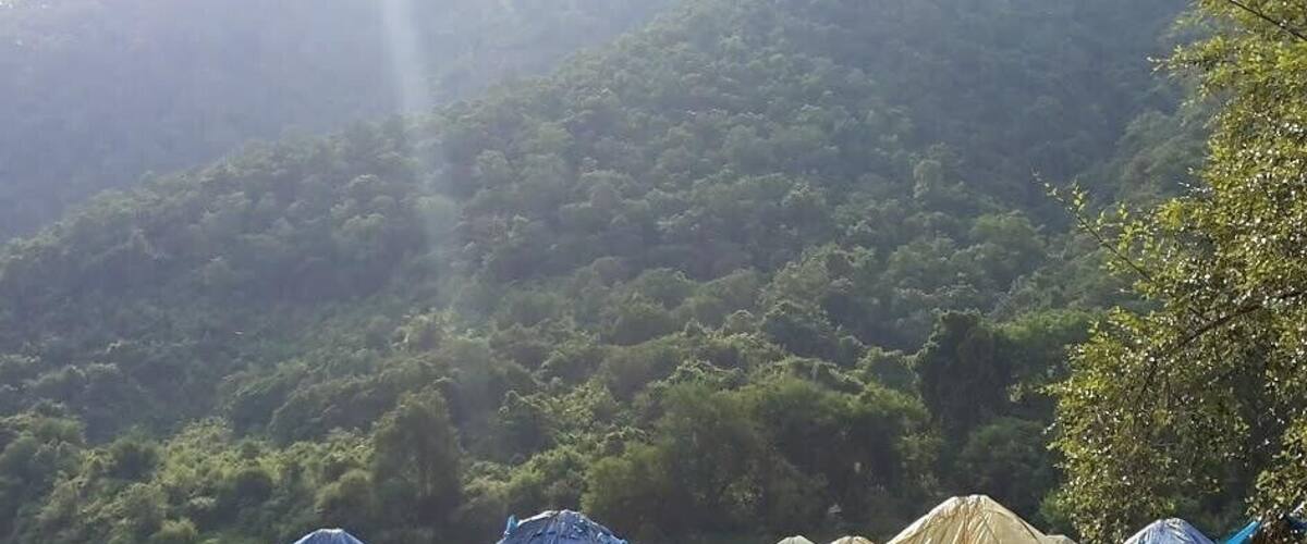 A campsite with several tents, surrounded by a forested hillside.