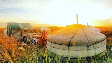 Uma yurta em um campo gramado com o pôr do sol ao fundo.