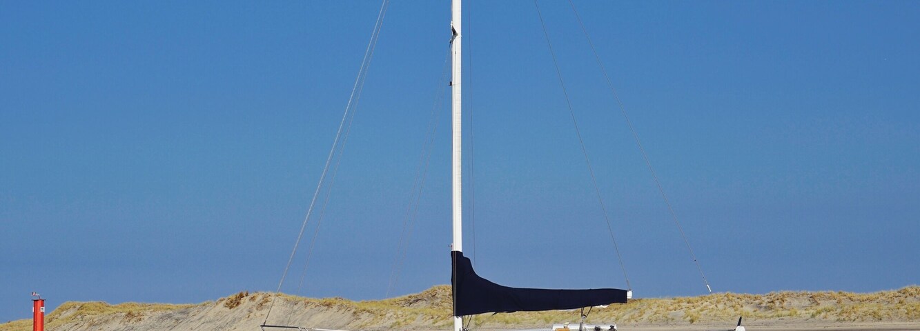 sailing yacht anchor in shallow water, sunny blue sky, oystercatcher in front, portrait.