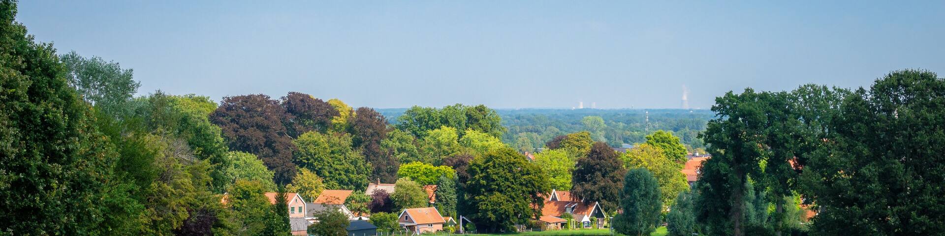 Standing in farmland of the region of Twente (province of Overijssel, The Netherlands) the outskirts of the village Ootmarsum in the front and the pipes of German industry in the back can be seen