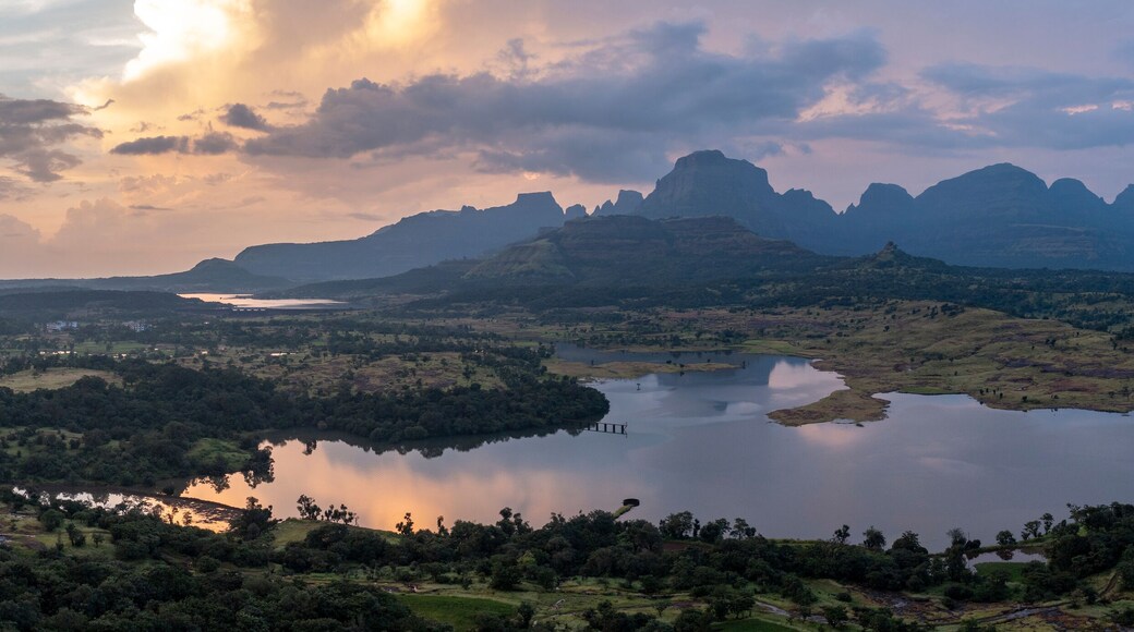 Aerial view of serene lake surrounded by majestic mountains and lush forest, Nashik district, India.