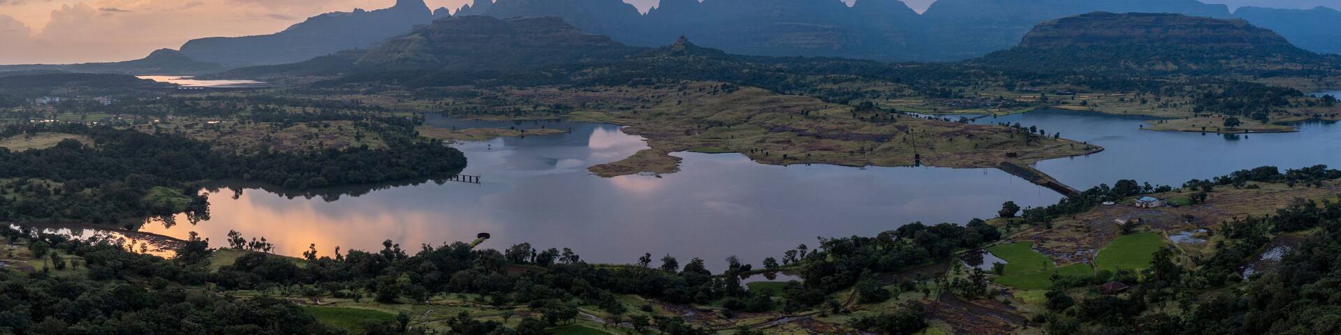 A mountainous landscape with a large lake surrounded by greenery and a few small buildings.