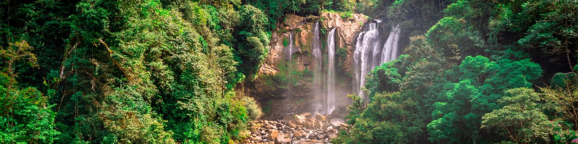 A multi-tiered waterfall surrounded by dense green forest.