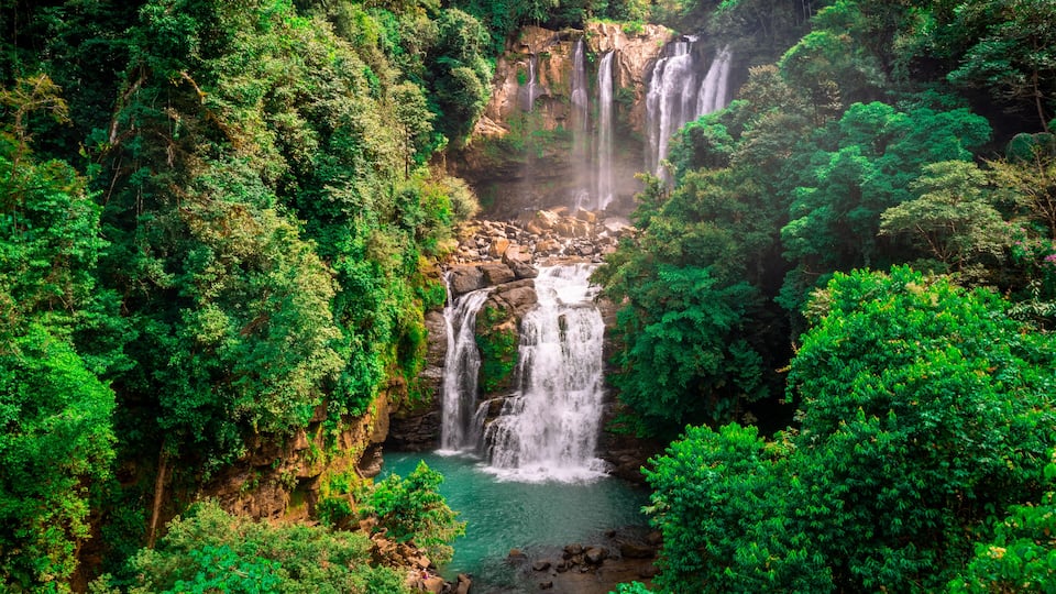 Ein mehrstufiger Wasserfall, umgeben von dichtem Grünwald.