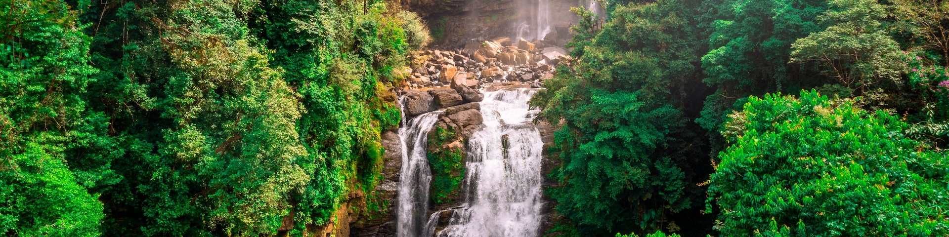 A multi-tiered waterfall surrounded by dense green forest.