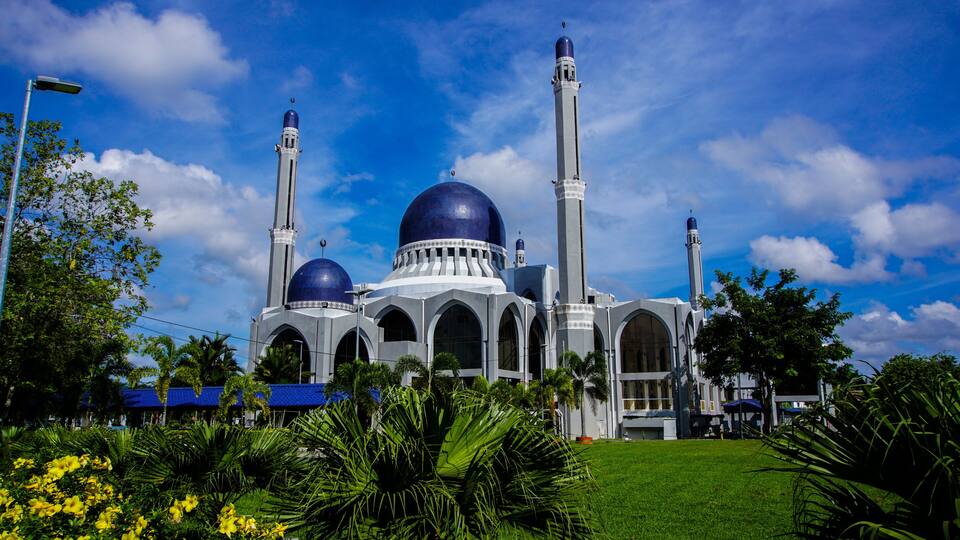 A mosque with two large domes and tall minarets, surrounded by greenery and a clear blue sky.