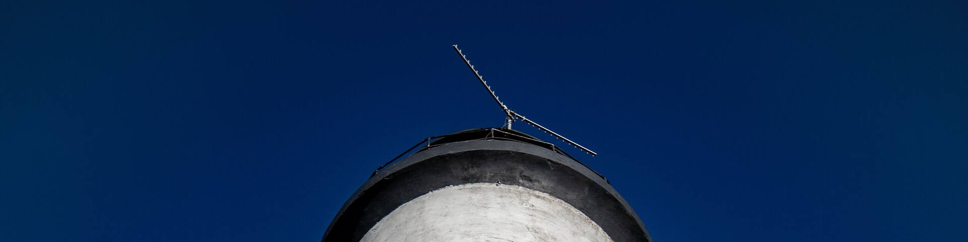 A tall lighthouse with alternating black and white stripes against a clear blue sky.