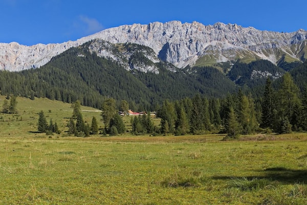 Eine Berglandschaft mit klarem Himmel, einer grünen Wiese und einem kleinen Gebäude in der Ferne.
