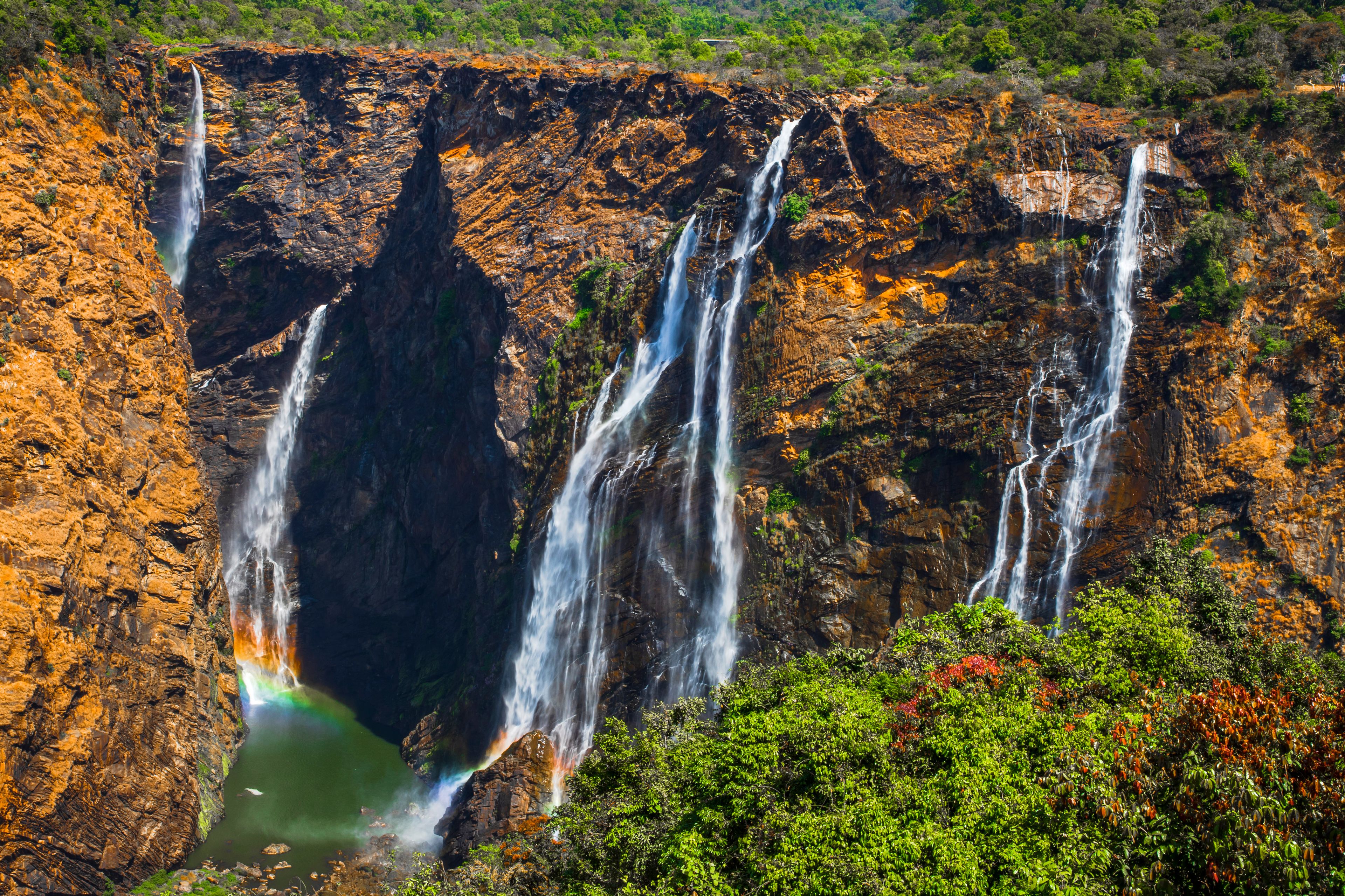 A multi-tiered waterfall cascading down a rocky cliff surrounded by lush greenery.